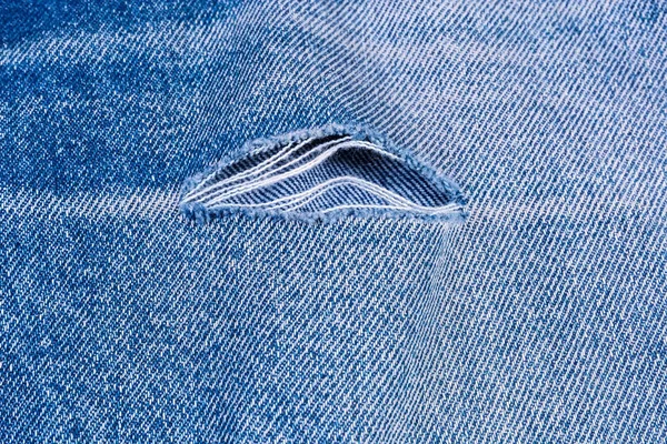 Buraco com fios desgastados em uma velha calça azul rasgada — Fotografia de Stock