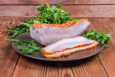 Partly sliced boiled smoked pork belly on dish with greens clipart