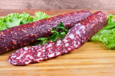 Kesme tahtası üzerinde marul ile kısmen dilimlenmiş kuru kürlenmiş sosis