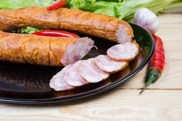 Partly sliced bologna sausage on dish among spices, vegetables