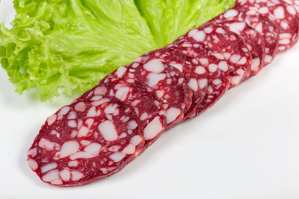 Sliced dry-cured sausage on dish with lettuce close-up — Stock Photo, Image