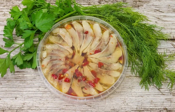 Pickled herring slices in container with spicy marinade, top view