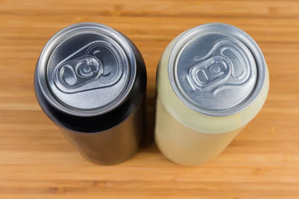 Top view of two different sealed beverage cans on wooden surface