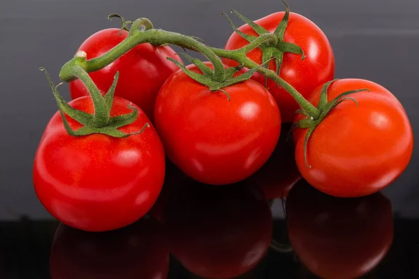 Los tomates rojos en la rama sobre la superficie oscura reflectante — Foto de Stock