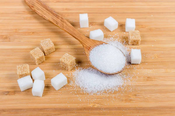 White sugar in wooden spoon, white and brown sugar cubes