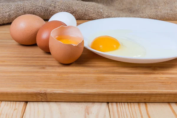 Huevos rotos y enteros sobre tabla de cortar sobre mesa rústica — Foto de Stock