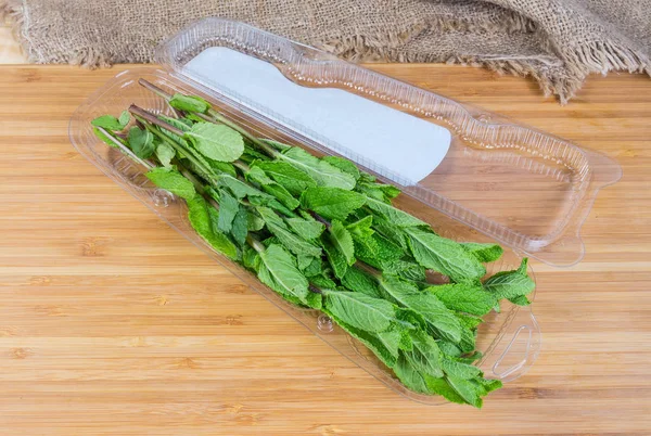 Fresh mint in the open plastic container on wooden surface — Stock Photo, Image