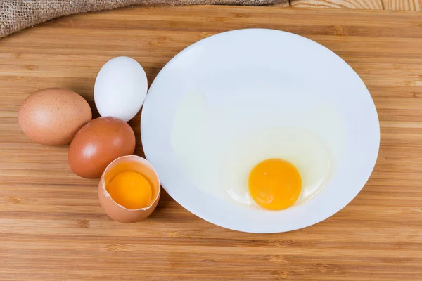 Huevos enteros y rotos en un plato sobre una superficie de madera — Foto de Stock