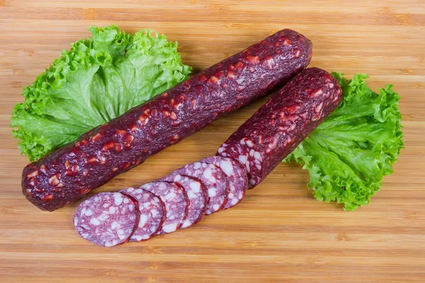 Embutidos parcialmente cortados en rodajas con lechuga en la tabla de cortar — Foto de Stock