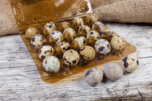 Quail eggs against of plastic packaging on old wooden surface — Stock Photo, Image