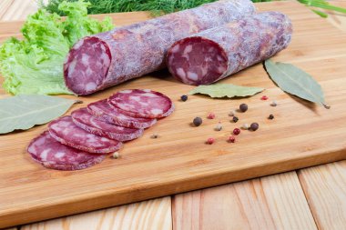 Kısmen dilimlenmiş kuru kürlenmiş sosis, yeşillik, kesme tahtası üzerinde baharatlar