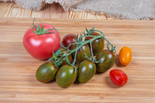 Différentes tomates cerises et tomate ordinaire sur planche à découper en bois — Photo