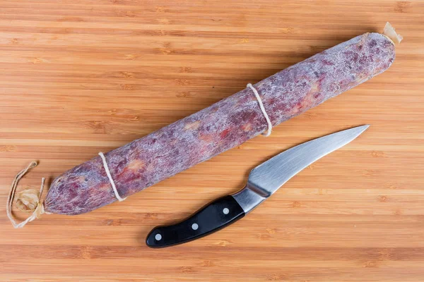 Salame inteiro e faca de cozinha na placa de corte de madeira — Fotografia de Stock