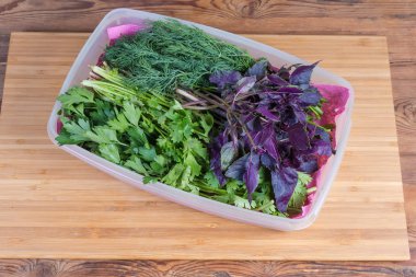 Bambu kesme tahtası üzerinde plastik kapta farklı taze yeşillikler