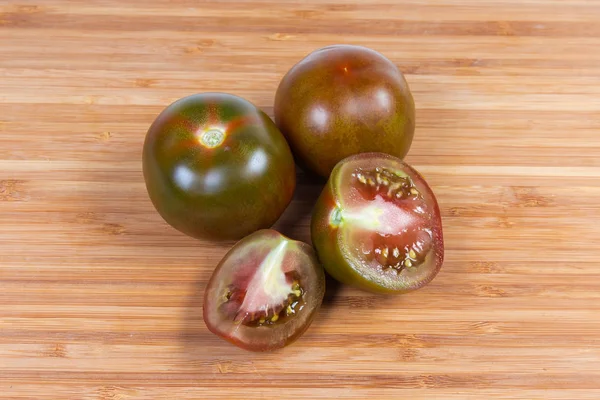 Tomates enteros y en rodajas kumato en la tabla de cortar — Foto de Stock