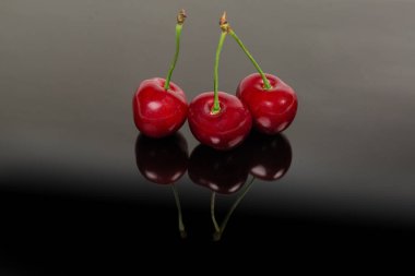 Koyu yansıtıcı yüzey üzerinde sapları ile üç kırmızı tatlı kiraz