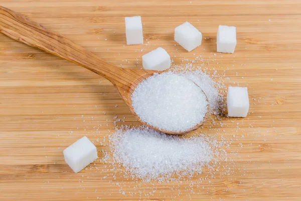 White sugar in wooden spoon and beside, white sugar cubes