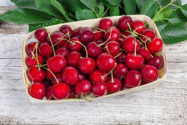 Sweet cherries in basket, leaves on the old wooden surface