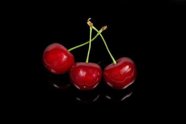 三个红色甜樱桃与茎在黑色反光表面 — 图库照片