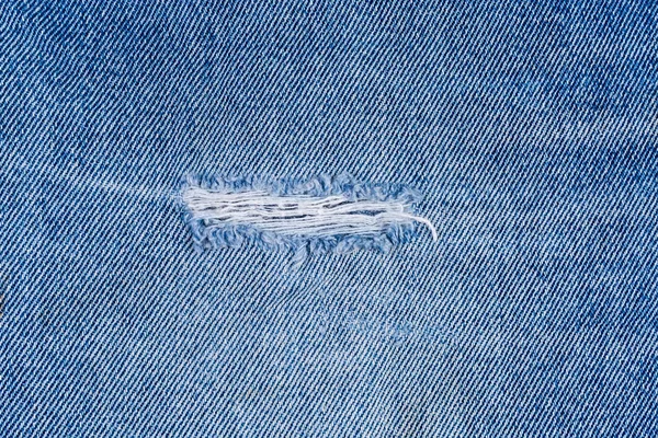 Gat met versleten draden in een oude gescheurde blauwe jeans — Stockfoto