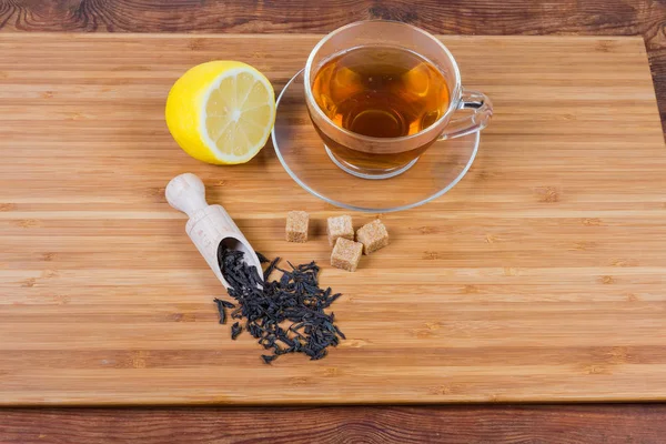 Svart teblad, tekopp och citron på träyta — Stockfoto