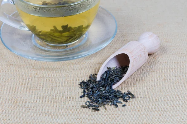Grönt te lämnar i trä krydda sked mot av Tea Cup — Stockfoto