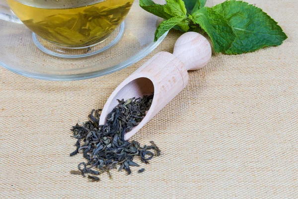 Dried green tea leaves among fresh mint, prepared tea cup