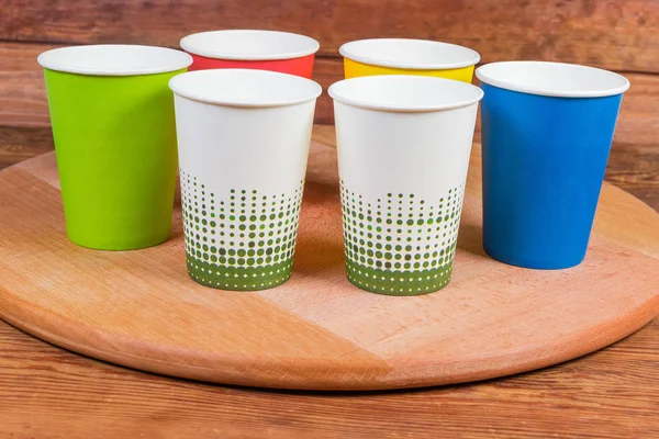 Disposable paper cups in different colors on wooden serving board