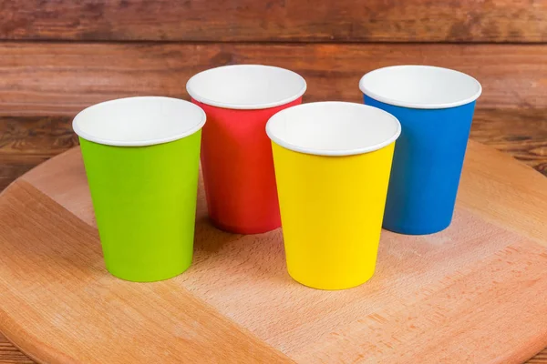 Disposable paper cups in different colors on wooden surface