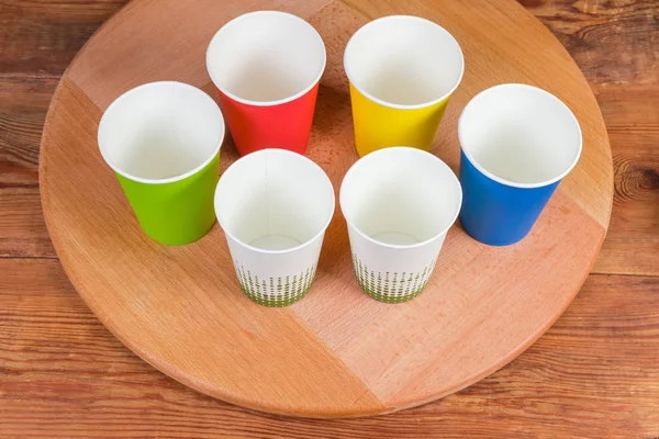 Tazas de papel desechables en diferentes colores en tablero de servir de madera — Foto de Stock