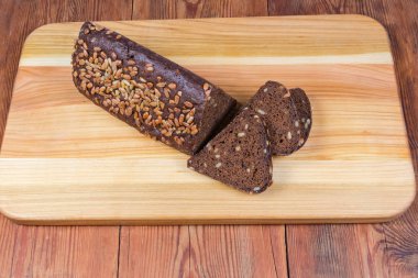 Ahşap kesme tahtası üzerinde kısmen dilimlenmiş kahverengi ekmek üçgen şeklinde