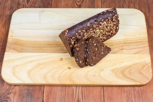 Ahşap kesme tahtası üzerinde kısmen dilimlenmiş kahverengi ekmek üçgen şeklinde