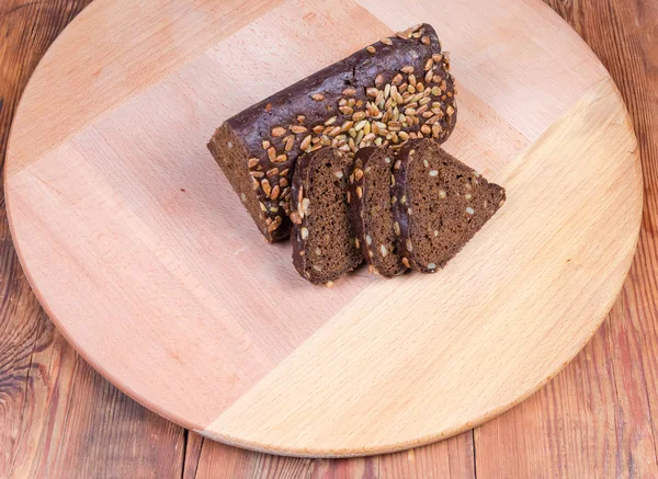 Ahşap servis tahtası üzerinde kısmen dilimlenmiş kahverengi ekmek üçgen şeklinde