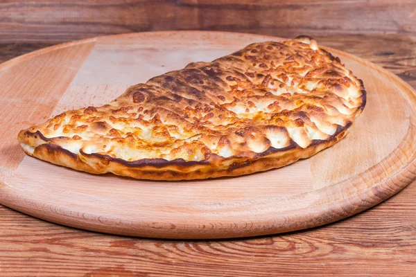 Gebackene Calzone-Pizza auf dem runden Servierbrett in Großaufnahme — Stockfoto