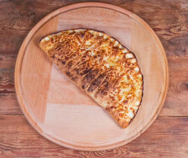Draufsicht auf gebackene Calzone-Pizza auf rundem Servierbrett — Stockfoto