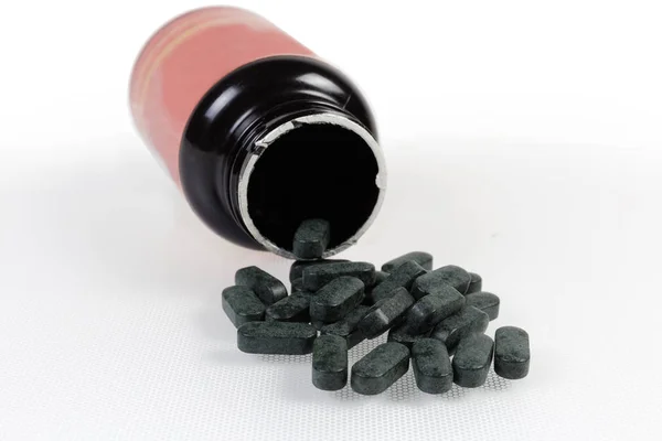 Ciemne tabletki suplementów diety na otwartym pojemniku — Zdjęcie stockowe