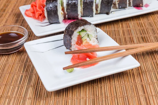 Sushi en platos rectangulares, condimentos, palillos en estera de mesa de bambú —  Fotos de Stock