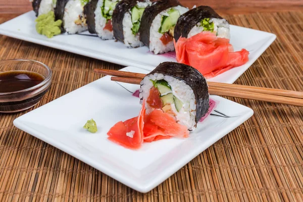 Sushi en platos, condimentos, palillos en la alfombra de mesa de bambú de cerca —  Fotos de Stock