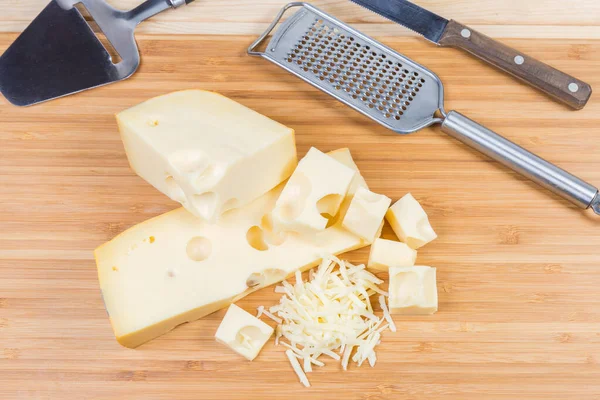 Gesneden en geraspte Zwitserse kaas en snijmachines op snijplank — Stockfoto