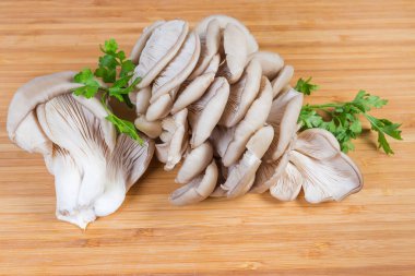 Tahtada çiğ istiridye mantarı ve maydanoz kümeleri.