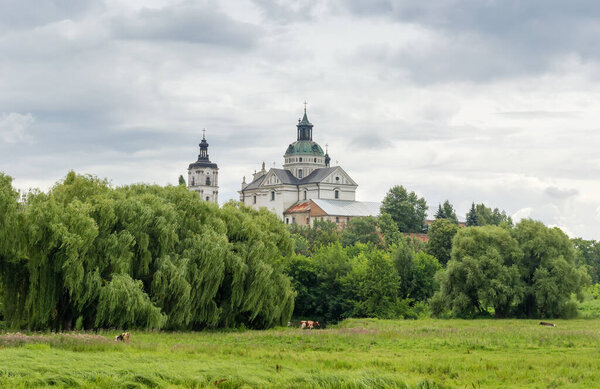Former fortified Monastery of the Order of Discalced Carmelites of the 17th century. General view with meadow and trees on a foreground in cloudy weather, Berdychiv, Ukraine