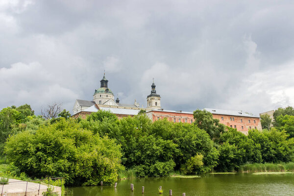 Former fortified Monastery of the Order of Discalced Carmelites of the 17th century. General view with water and trees on a foreground in cloudy weather, Berdychiv, Ukraine