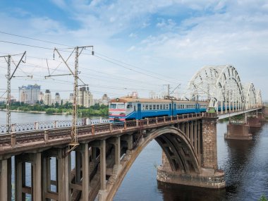 Şehir elektrikli çoklu tren nehir üzerindeki kemer demiryolu köprüsüne hareket ediyor. Darnytskyi Demiryolu Köprüsü Dinyeper Nehri, Kyiv, Ukrayna