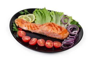 Izgara alabalık filetosu, sebze ve sebzeyle birlikte beyaz arka planda, siyah tabakta servis edilir.