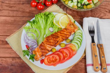 Sebze ve sebzeli ızgara alabalık filetosu ve kırsal masadaki çatal bıçak seti.