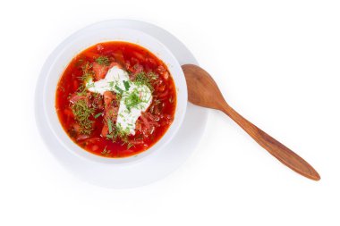 Tipik kırmızı pancar çorbası, ekşi krema ve taze kesilmiş otlarla tatlandırılmış, beyaz arka planda ahşap kaşıkla servis edilmiş, üst manzara.