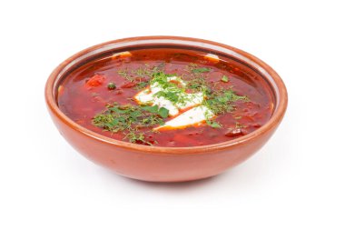Tipik kırmızı pancar çorbası, ekşi kremayla tatlandırılmış ve beyaz arka planda seramik kasede servis edilen taze doğranmış otlarla serpilmiş.