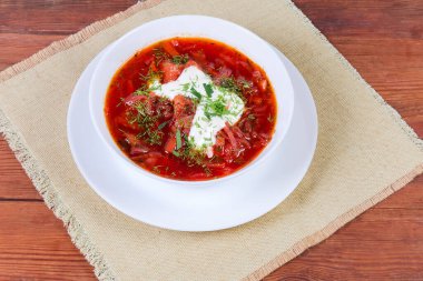 Tipik kırmızı pancar kökü Ukrayna çorbası ekşi kremayla tatlandırılmış ve kırsal masadaki peçetede servis edilen taze doğranmış otlarla serpiştirilmiş.