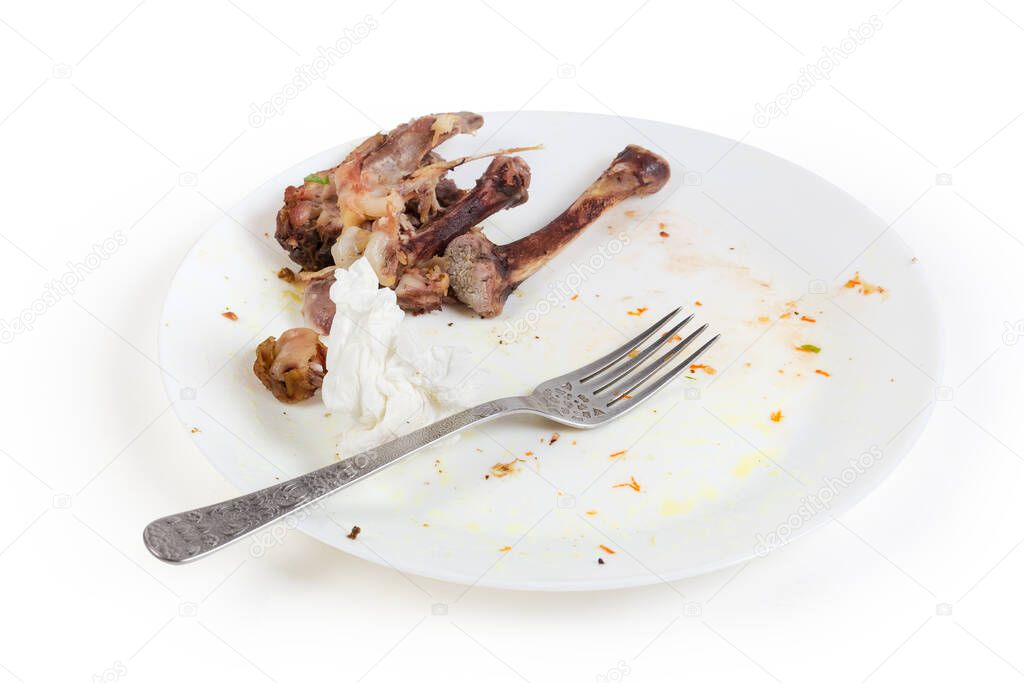 Dirty plate after eating with gnawed chicken leg bones, used paper napkin and fork on a white background