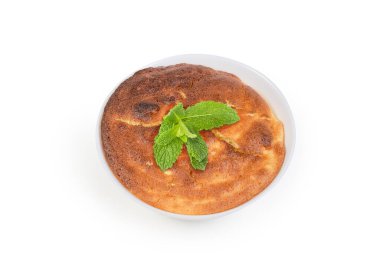 Beyaz arka plandaki küçük beyaz kâsede naneli yaprak ile süslenmiş fırında lor suflesi.